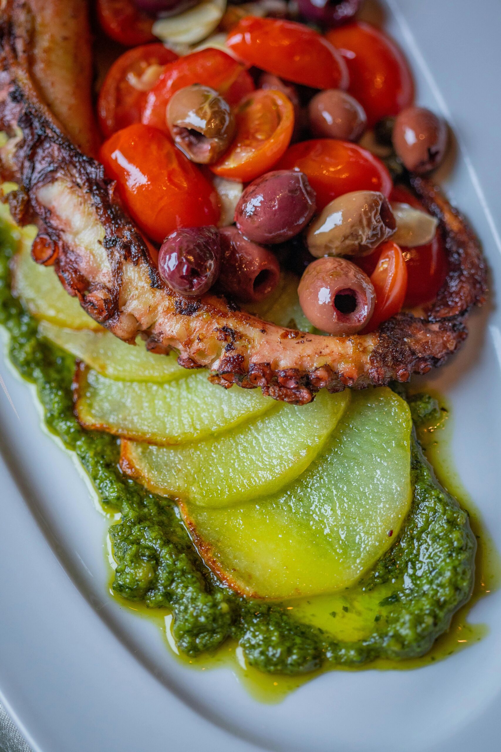 pexels-photo-10038710-10038710 Delicious octopus dish with cherry tomatoes, olives, and pesto sauce on a white plate.
